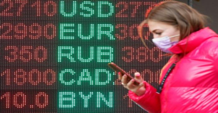 FILE PHOTO: A woman walks past a board showing currency exchange rates in Kiev
