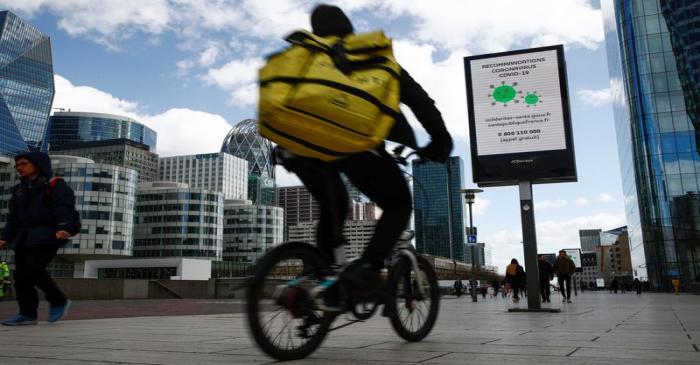 People walk pass a board with information about coronavirus (COVID-19) at the financial and