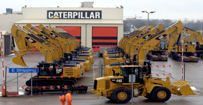 FILE PHOTO: Workers walk past Caterpillar excavator machines at a factory in Gosselies