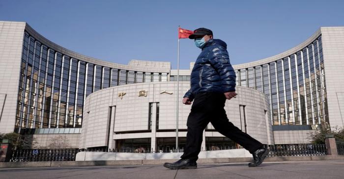 Man wearing a mask walks past the headquarters of the People's Bank of China, the central bank,