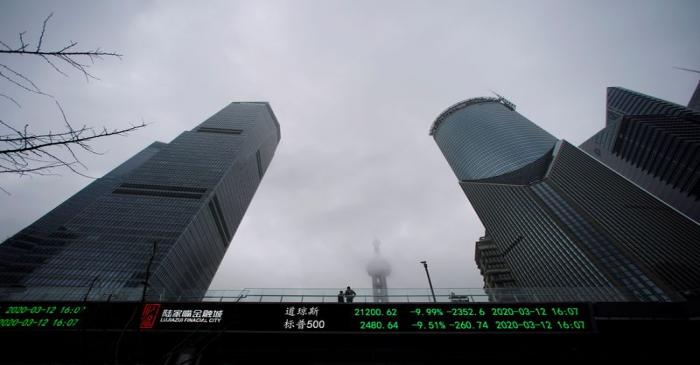 People are seen on a pedestrian overpass with an electronic board showing the Dow Jones and S&P