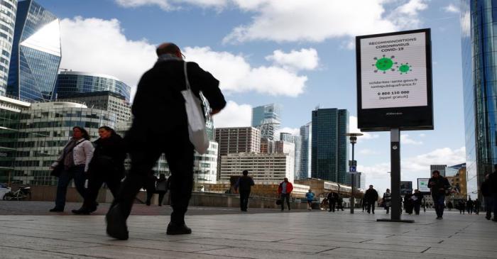 People walk pass a board with information about coronavirus (COVID-19) at the financial and