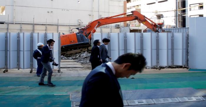 FILE PHOTO: Businessmen walk past heavy machinery at a construction site in Tokyo's business