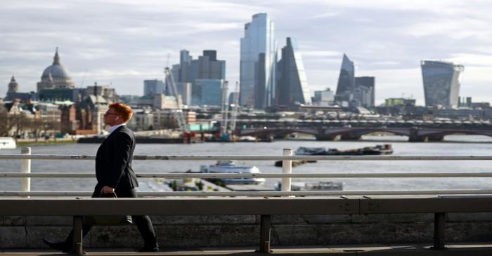 A man walks across Waterloo Bridge in front of the City of London financial district during