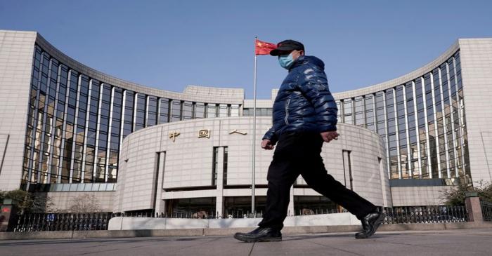 FILE PHOTO: Man wearing a mask walks past the headquarters of the People's Bank of China, the