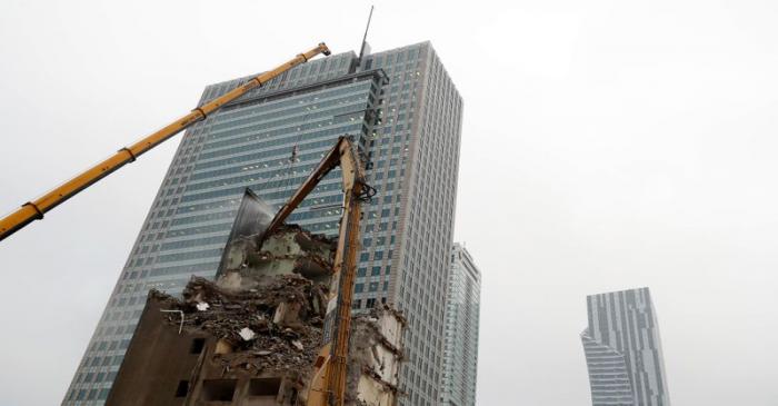 An excavator demolishes a building near skyscrapers in the centre of Warsaw