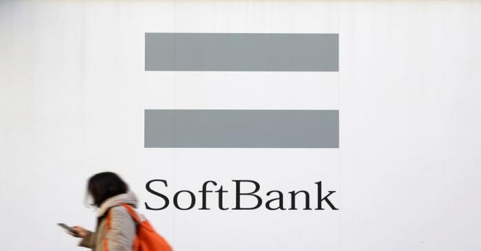 FILE PHOTO: A woman using a mobile phone walks past the logo of SoftBank Corp in Tokyo