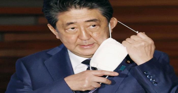 Japan's Prime Minister Shinzo Abe taking off his face mask as he arrives to speak to the media