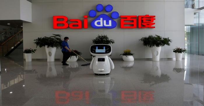 FILE PHOTO: Worker wearing a face mask cleans the floor, near a Baidu AI robot which shows a