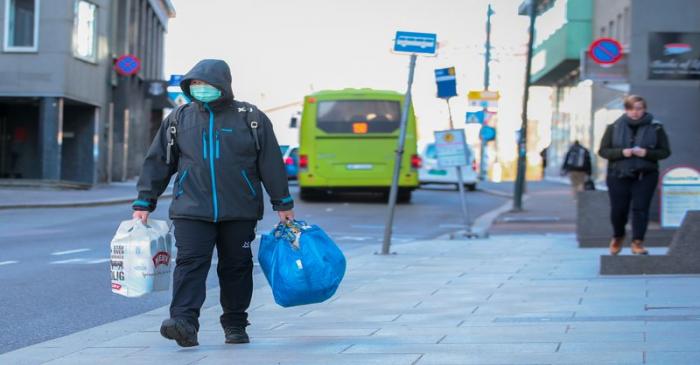 A man wearing a protective mask carries shopping bags as he walks on the streets of Oslo