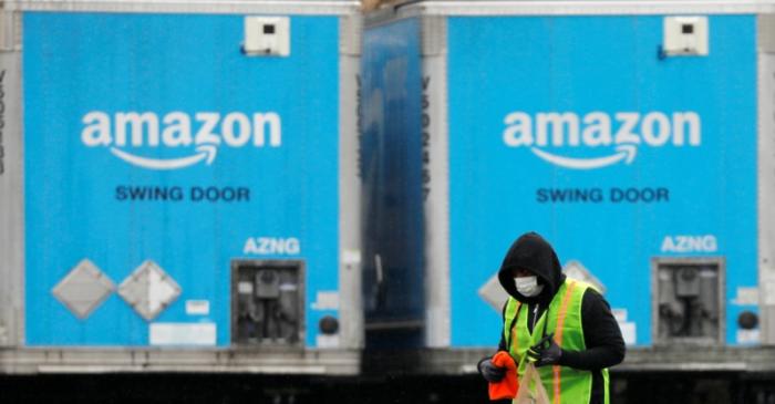 A worker in a face mask walks by trucks parked at an Amazon facility as the global coronavirus