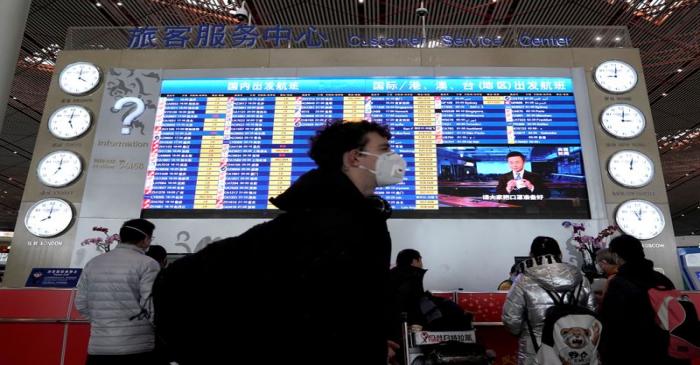 FILE PHOTO: A foreign traveller wearing a mask walks past a departures information board at