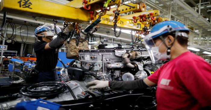 Employees wearing protective face masks and face guards work on the automobile assembly line