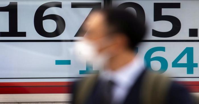 A man wearing a protective face mask walks past a screen showing Nikkei index outside a