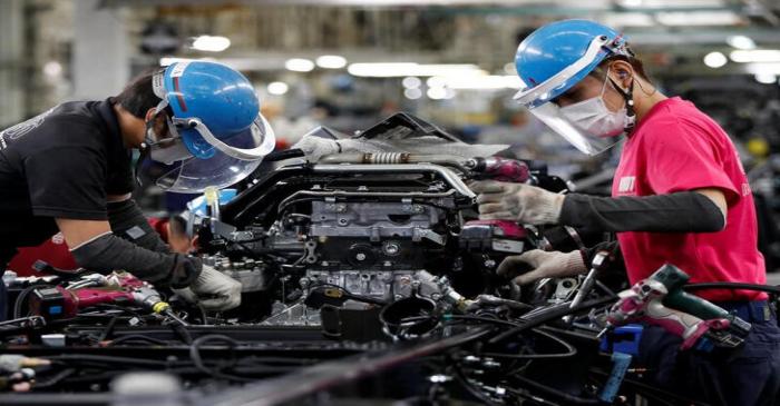 Employees wearing protective face masks and face guards work on the automobile assembly line