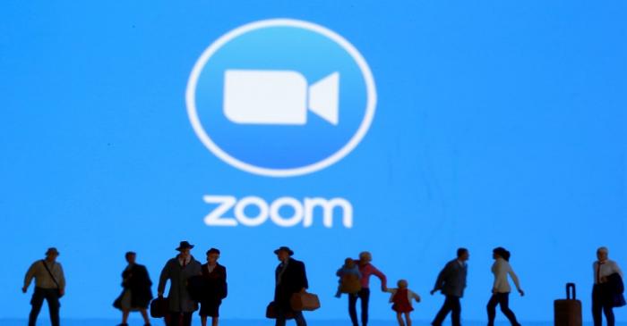 Small toy figures are seen in front of diplayed Zoom logo