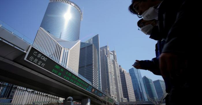 Pedestrians wearing face masks walk near an overpass with an electronic board showing stock