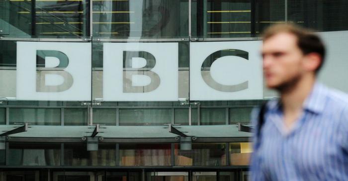 A pedestrian walks past a BBC logo at Broadcasting House in central London