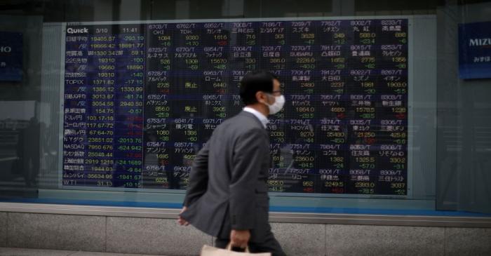 A man wearing protective face mask walks in front of a stock quotation board outside a