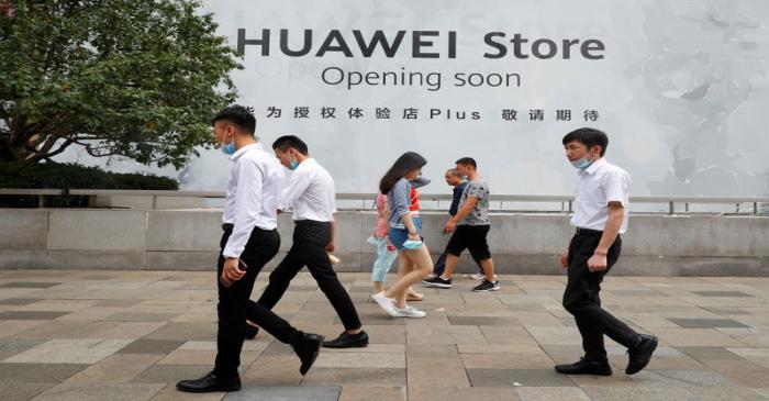 People walk past an advertisement announcing the opening of a HUAWEI store in Beijing