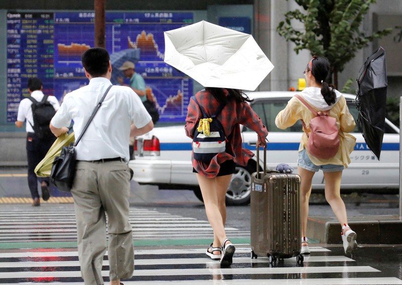 Passersby using umbrellas struggle against a heavy rain and wind in front of an electronic