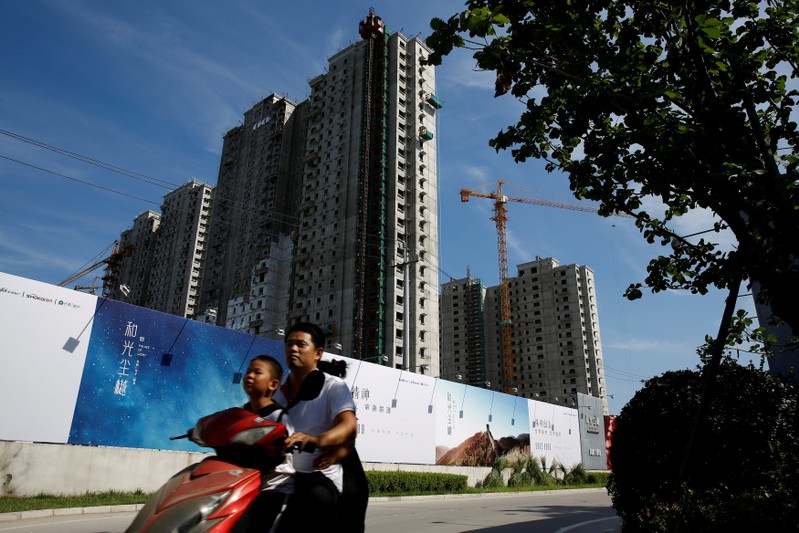 FILE PHOTO: A man and a boy ride an electric scooter past the shells of apartment blocks