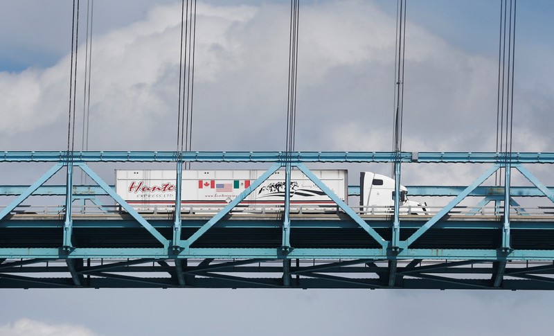A commercial truck with a Canada, United States and Mexico flag on its side is seen crossing