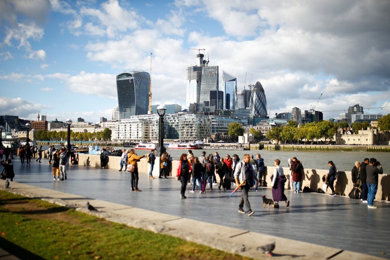 People walk by the River Thames across from the financial district of London
