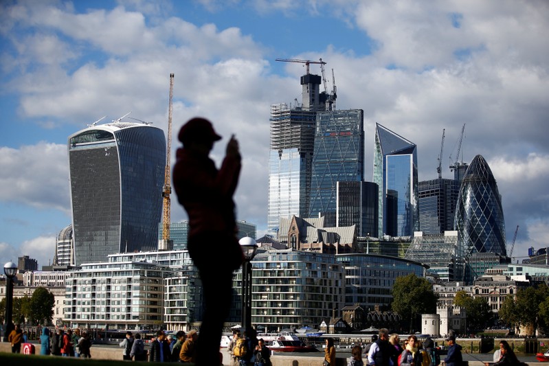A person takes a photograph with the financial district in the background, in London