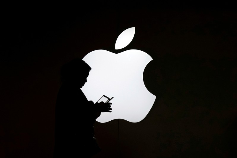A woman looks at the screen of her mobile phone in front of an Apple logo outside its store in