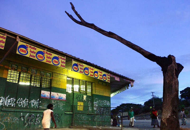 FILE PHOTO: Local residents walk past a heavily secured store with a dead tree arching over