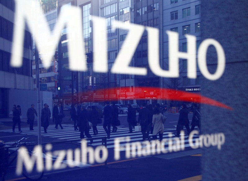 FILE PHOTO: Pedestrians are reflected on Mizuho Bank's signboard in Tokyo