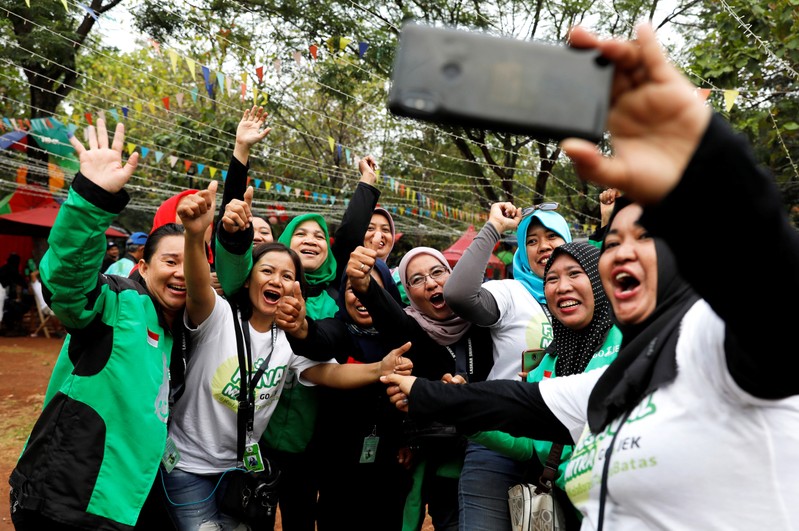 Women Gojek drivers react as they take pictures during Go-Food festival in Jakarta