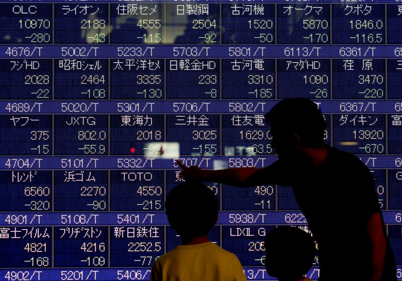 A man talks to his children in front of an electronic stock quotation board outside a brokerage