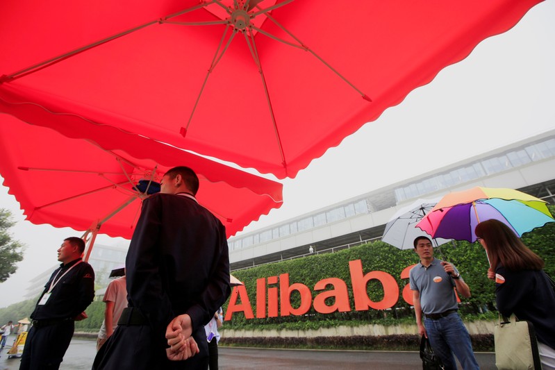 FILE PHOTO: People stand near a sign of Alibaba Group at its campus in Hangzhou