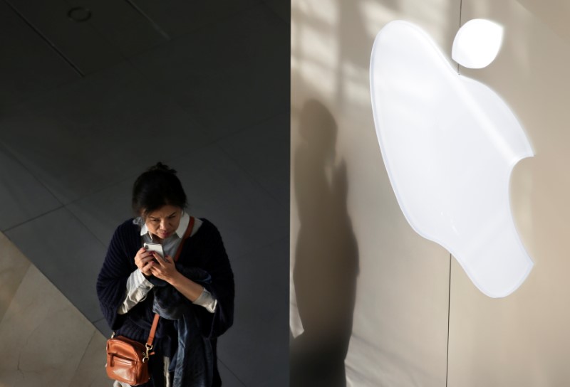 A woman holds her phone near an Apple company logo in Beijing