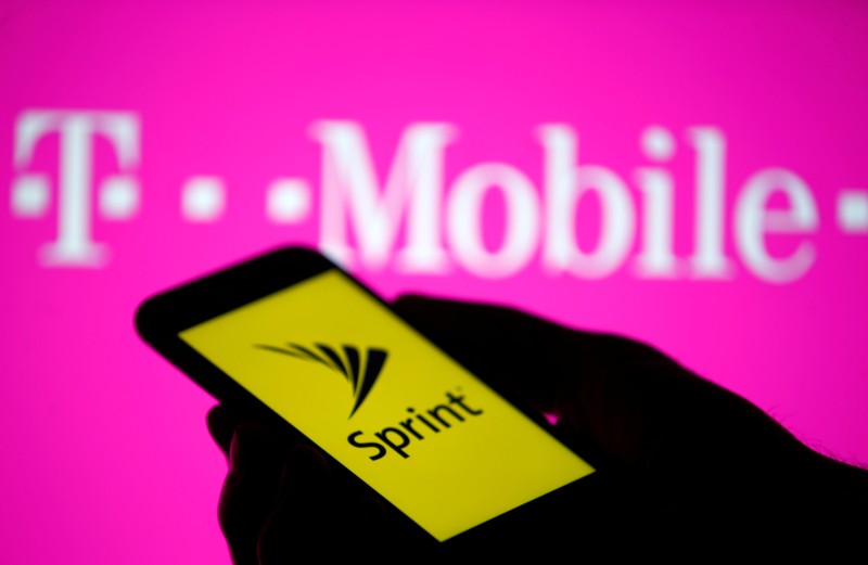 A smartphone with Sprint logo are seen in front of a screen projection of T-mobile logo, in