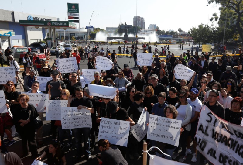 People hold posters as they take part in a protest against fuel shortages near a gas station in