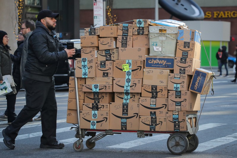 A delivery person pushes a cart full of Amazon boxes in New York