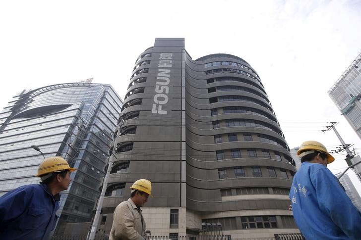 Construction workers walk past a building of the headquarters of Fosun International, in