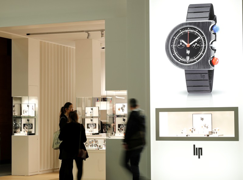 People walk past the exhibition stand of French manufacturer LIP at the Baselworld watch and