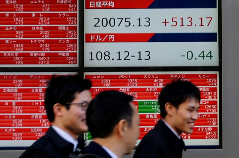 Pedestrians walk past electronic board showing the Nikkei stock index outside a brokerage in