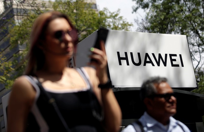 FILE PHOTO:  People walk past a Huawei company logo at a bus stop in Mexico City