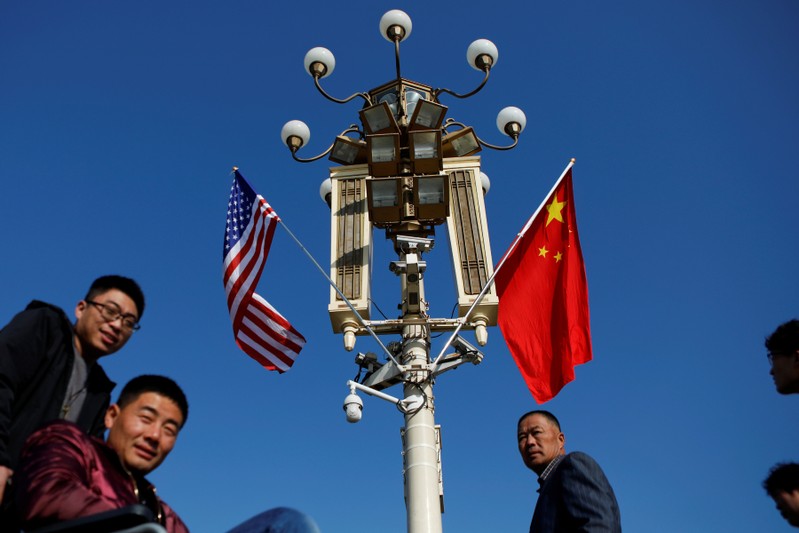 People pass a pole with security cameras, U.S. and China's flags near the Forbidden City ahead