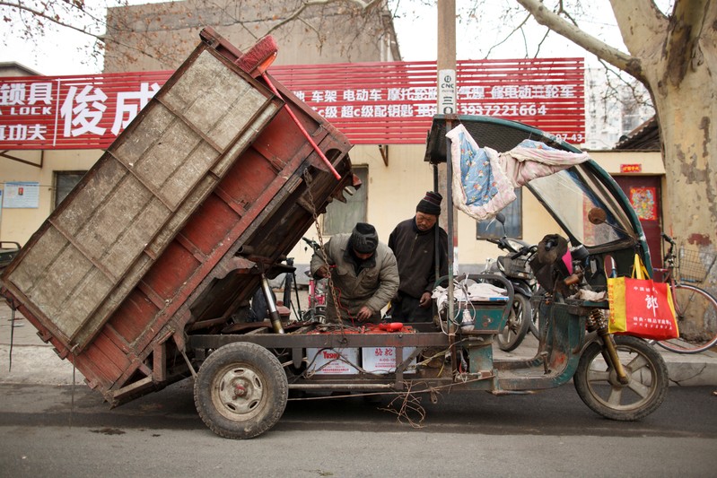 Wang Junchang replairs an electric vehicle at their worshop opposite a steel plant in Anyang