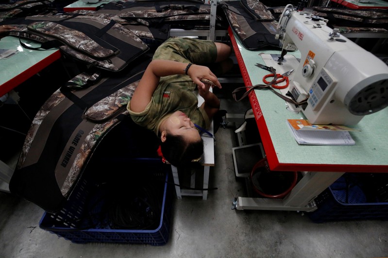 A worker plays with her phone during her lunch break at Yakeda Outdoor Travel Products Co. LTD