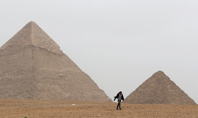 FILE PHOTO: A man walks in front of the Great Pyramids in Giza, on the outskirts of Cairo