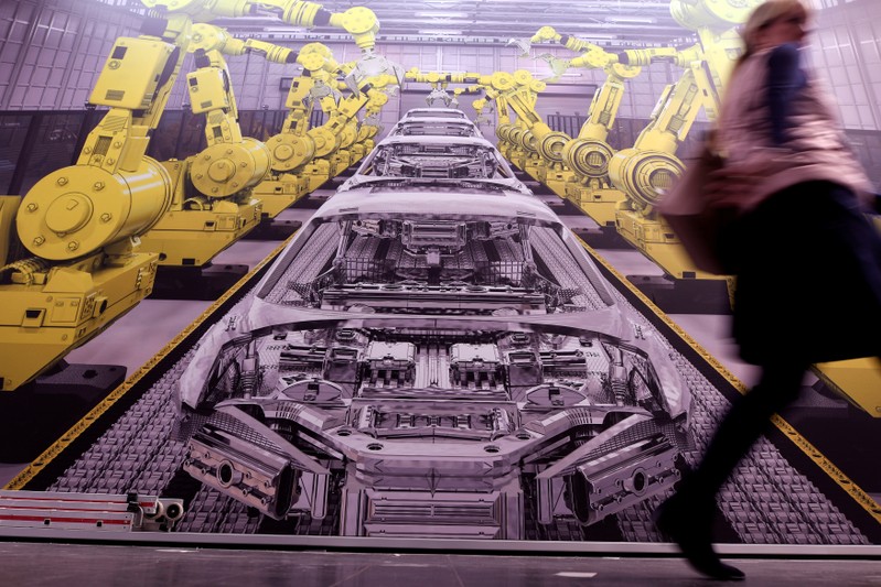 FILE PHOTO: A woman passes a poster showing a production line with robots at the Hanover trade