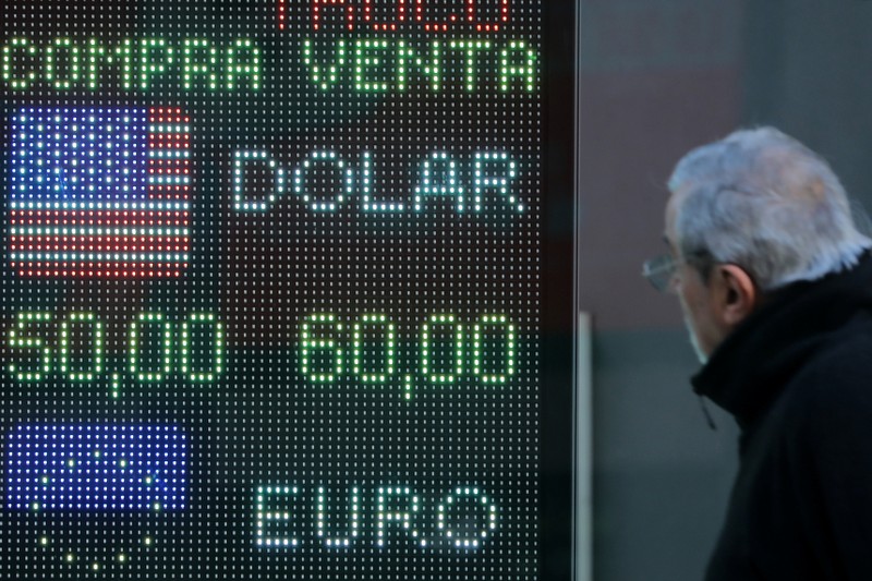 A man looks at an electronic board showing currency exchange rates in Buenos Aires' financial