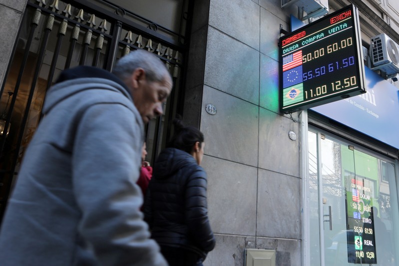 Pedestrians walk past an electronic board showing currency exchange rates in Buenos Aires'
